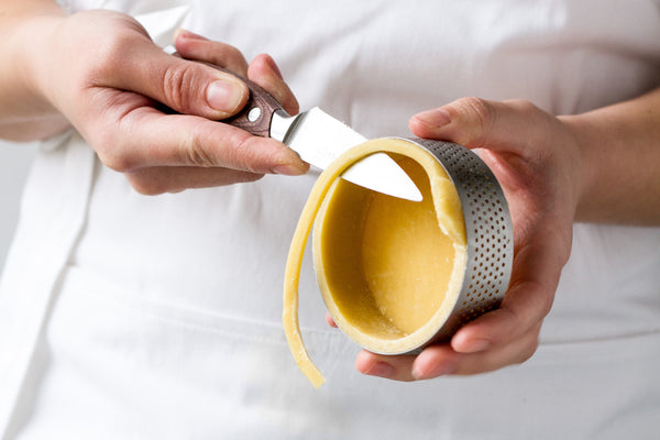 Pastry chef trimming tart shell in perforated ring